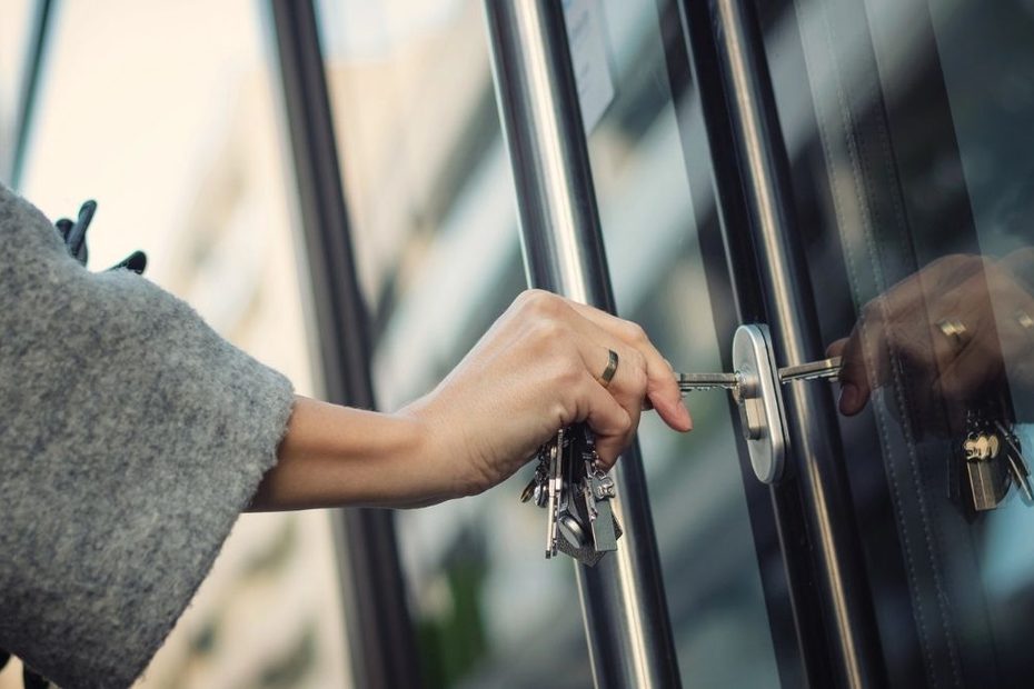 Trebuie încuiată ușa de la bloc noaptea? În imagine, o femeie care încuie ușa unui imobil cu cheia