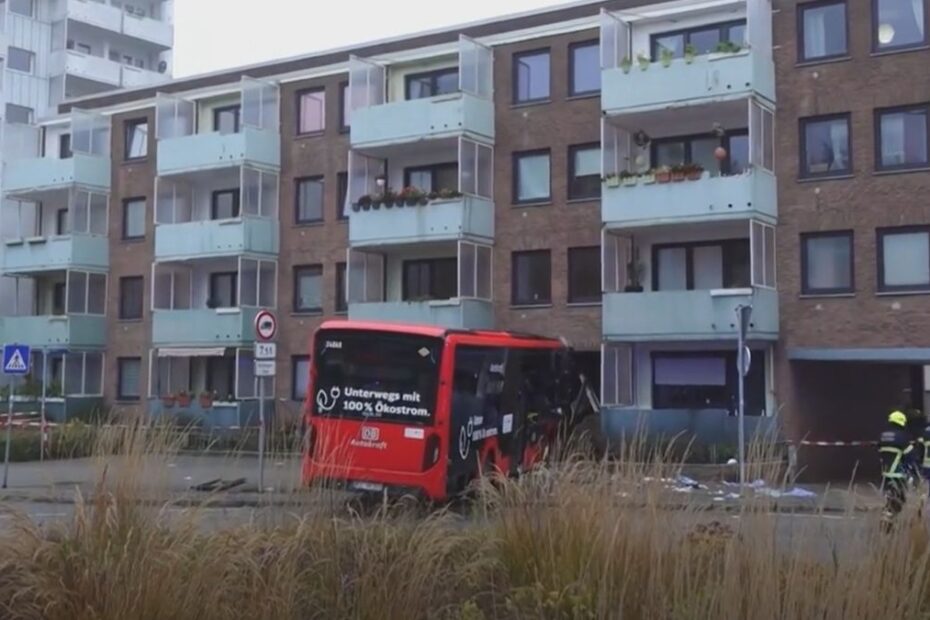 Autobuz roșu intrat în fațada unui bloc de locuințe din Bad Oldesloe, lângă echipajele de intervenție