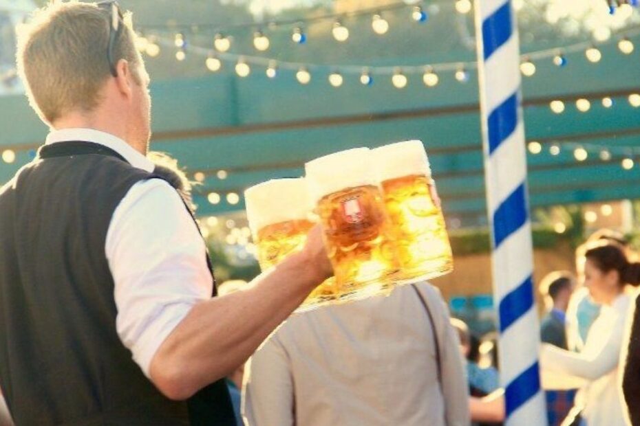 Chelner la Oktoberfest transportând mai multe halbe cu bere printre participanții dintr-un cort al festivalului