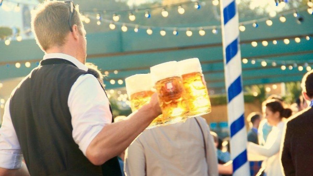 Chelner la Oktoberfest transportând mai multe halbe cu bere printre participanții dintr-un cort al festivalului