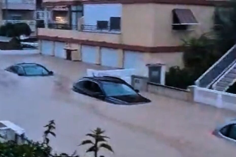Autoturisme aproape acoperite de apă pe o stradă cu locuințe din Spania