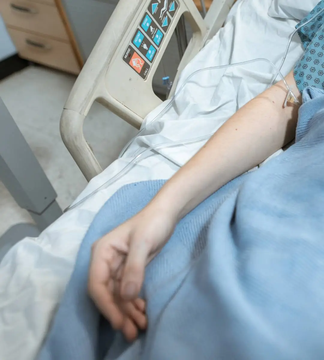 Brațul unui pacient cu perfuzie, întins într-un pat de spital