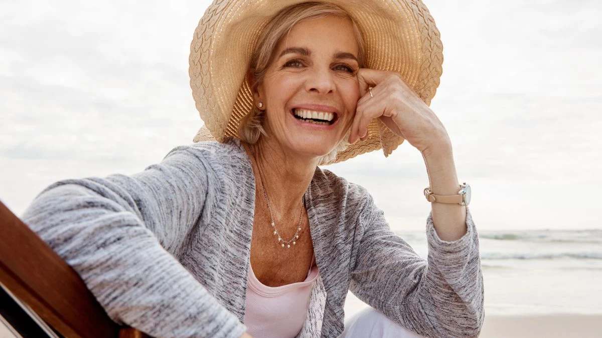 Femeie pensionară zâmbitoare, cu pălărie de paie, relaxându-se pe malul mării, imagine ilustrativă pentru cele mai bune țări în care să trăiești la pensie în 2026.