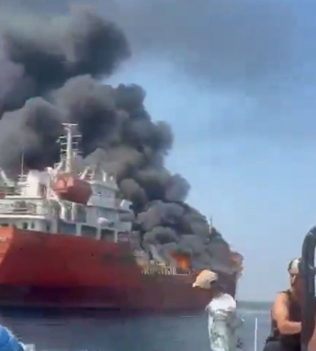 Petrolier cuprins de flăcări pe mare, cu nori uriași de fum negru ridicându-se deasupra navei, în timp ce mai multe persoane privesc incendiul de pe o ambarcațiune din apropiere.