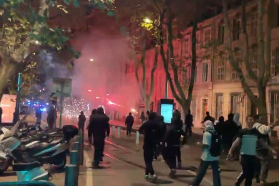 Grupuri de persoane pe o stradă noaptea, printre fum și lumini roșii, în timpul protestelor