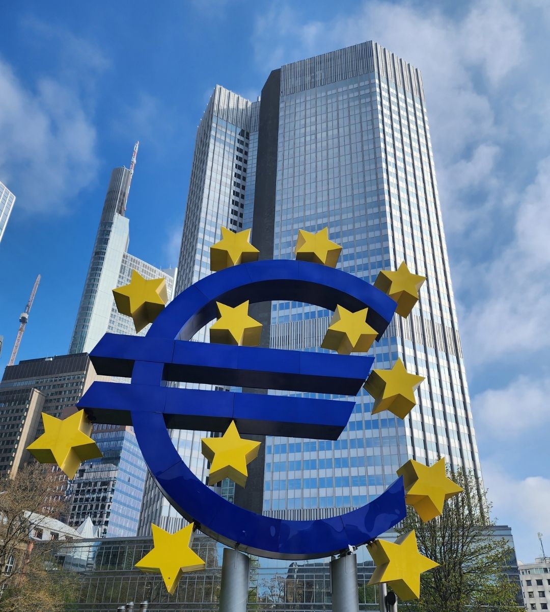 Sculptura monumentală a simbolului euro, înconjurată de stele galbene, în fața clădirii Eurotower din Frankfurt, fostul sediu al Băncii Centrale Europene.