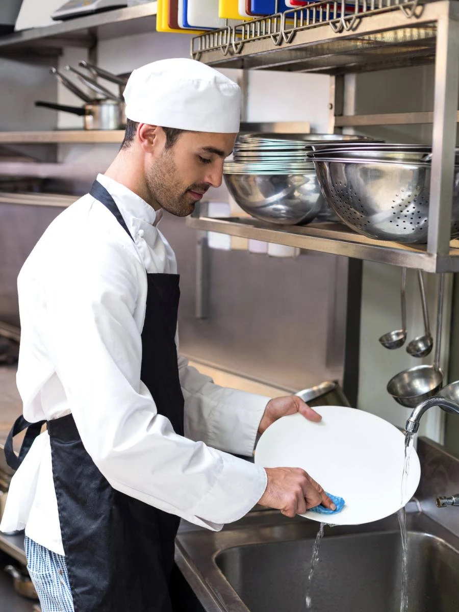 Un bărbat spală manual o farfurie într-o bucătărie de restaurant