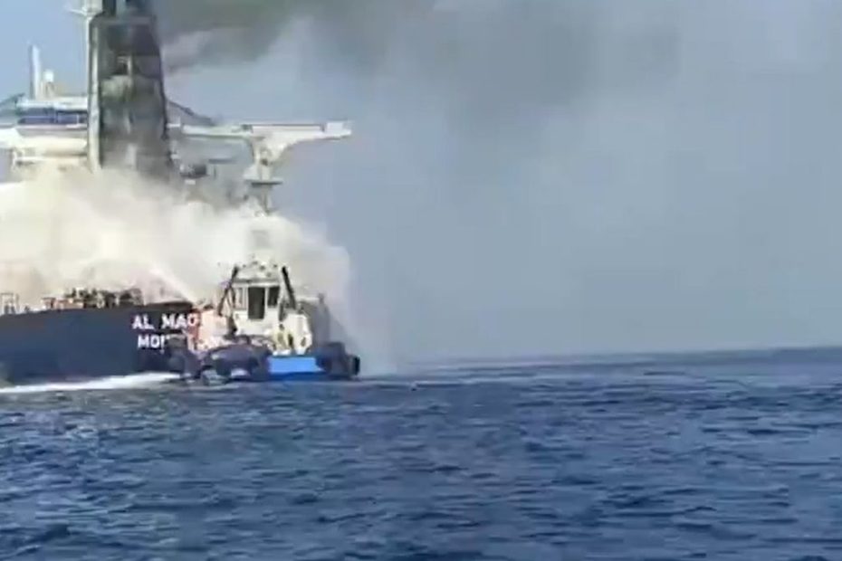 Petrolier cuprins de flăcări și fum negru pe mare, în timp ce o ambarcațiune de intervenție pulverizează apă pentru stingerea incendiului.