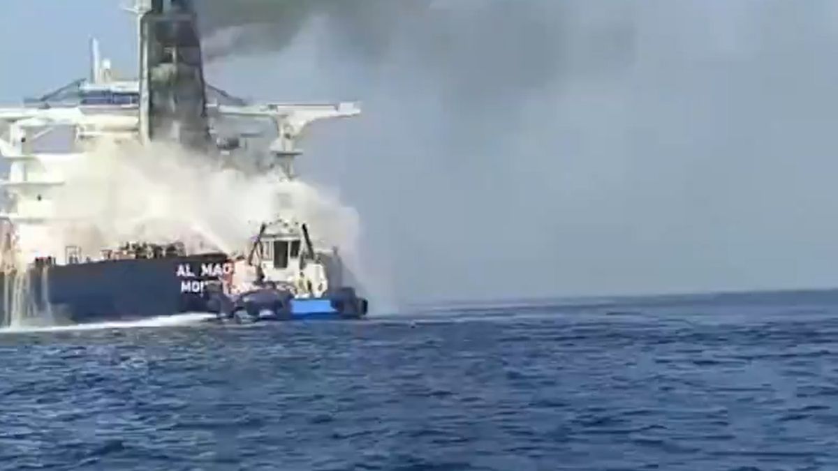 Petrolier cuprins de flăcări și fum negru pe mare, în timp ce o ambarcațiune de intervenție pulverizează apă pentru stingerea incendiului.